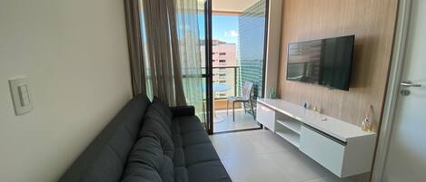 A modern living room with a black sofa, a white TV stand, and a sliding glass door leading to a balcony.