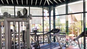 Een fitnessruimte met loopbanden en krachtapparaten, grote ramen met uitzicht op palmbomen en gebouwen.