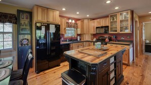 Una cocina con armarios de madera, un refrigerador negro, un microondas y una isla de madera con tabla de cortar.