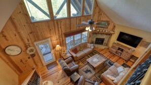 Interior acogedor de una cabaña con chimenea, sofás de cuero, televisor y un ventanal con vistas al exterior.
