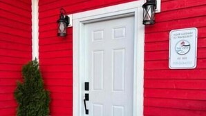 Une maison rouge avec une porte blanche, un paillasson noir et une enseigne sur le mur.