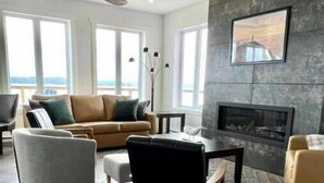 Un salon moderne avec un canapé, des fauteuils, une cheminée et une vue dégagée grâce à de grandes fenêtres.