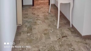 Un couloir avec un sol carrelé, une porte blanche, une table blanche ornée d’un pot de plantes et un miroir fixé au mur.