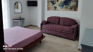 Une chambre à coucher avec un lit, un canapé, une petite table, un téléviseur et une carte du monde accrochée au mur.