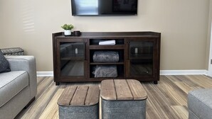 Una sala de estar con un mueble de madera oscura, un televisor de pantalla plana montado encima y dos taburetes metálicos al frente.