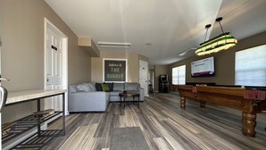 Una sala de estar amplia con un sofá gris, una mesa de centro, una mesa de billar y una lámpara colgante.
