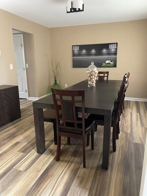 A dining room with a dark wooden table, chairs, a vase with branches, and a sports-themed wall hanging.