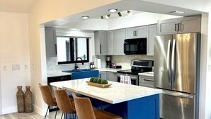 A modern kitchen with a central island, stainless steel appliances, and a blue accent wall. - WELCOME- MARCO ISLAND BEACH LIFEISGOOD STYLISH HOME! FOOD, FUN, SUN & MEMORIES! (Marco Island)