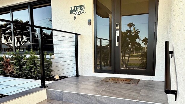 A modern building entrance with a glass door, a metal staircase, and a small outdoor area with plants. - WELCOME- MARCO ISLAND BEACH LIFEISGOOD STYLISH HOME! FOOD, FUN, SUN & MEMORIES! (Marco Island)