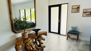 A spacious room with a large mirror, a wooden console table, a bench, and a door leading to an outdoor area. - WELCOME- MARCO ISLAND BEACH LIFEISGOOD STYLISH HOME! FOOD, FUN, SUN & MEMORIES! (Marco Island)