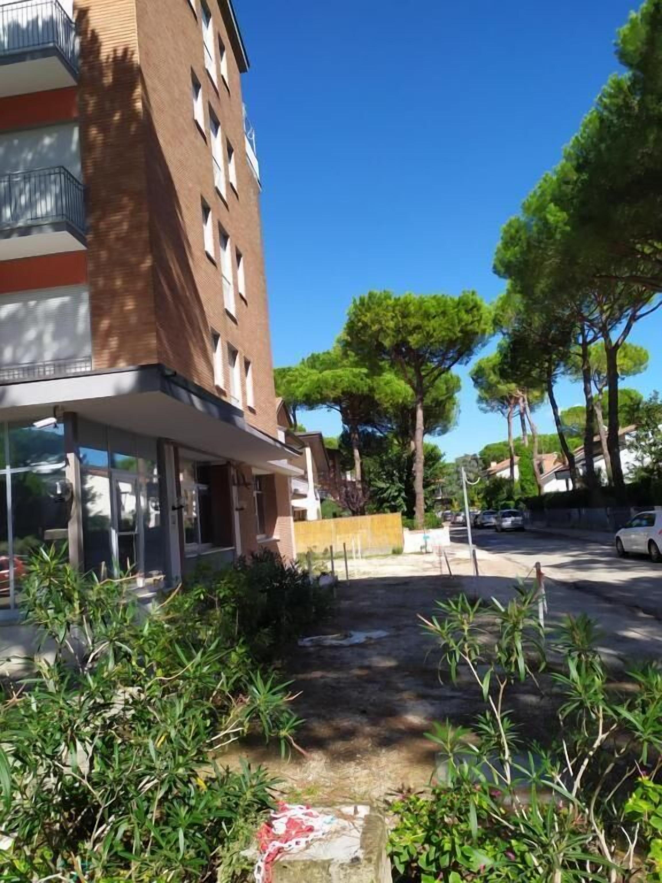 Un edificio de varios pisos con un acceso cubierto y un patio empedrado con árboles.