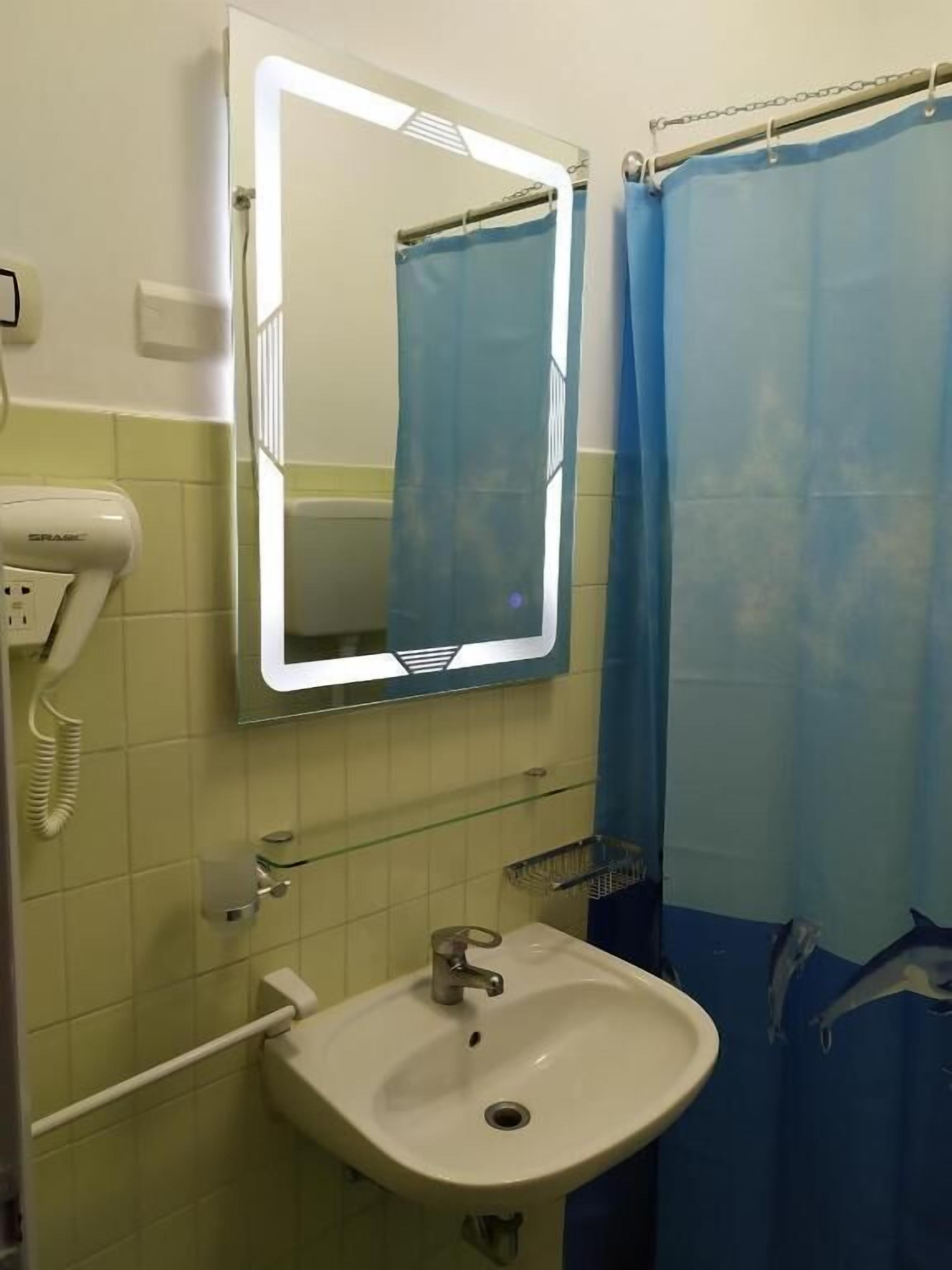 Un baño con un lavamanos blanco, un espejo, una cortina de ducha azul y un secador de manos.