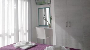 Een slaapkamer met een bed, een bureau, een stoel, een kledingkast en een televisie aan de muur.