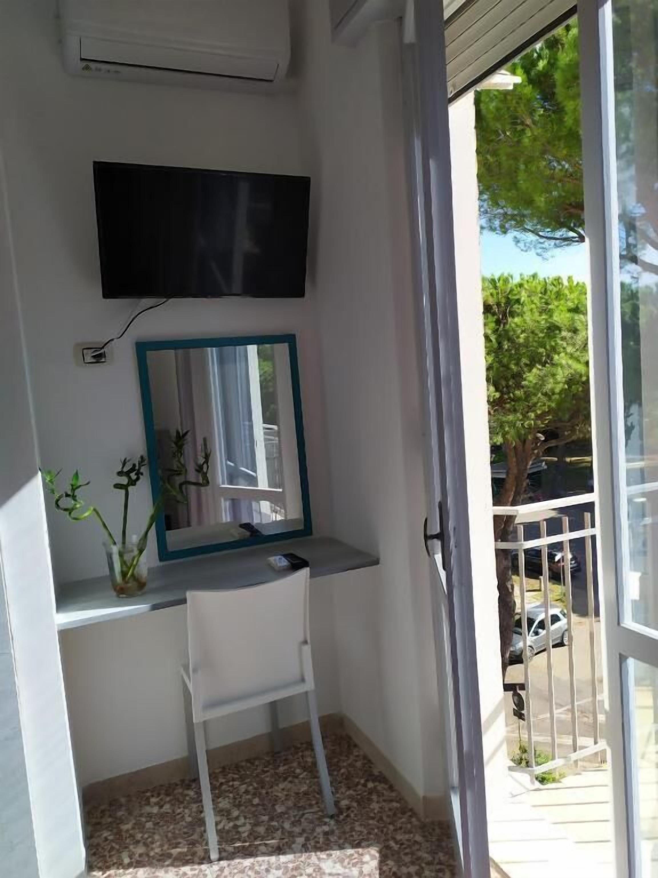 Un pequeño balcón con una silla blanca, un espejo y un televisor instalado en la pared.