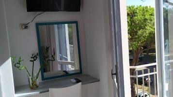 Un pequeño balcón con una silla blanca, un espejo y un televisor instalado en la pared.