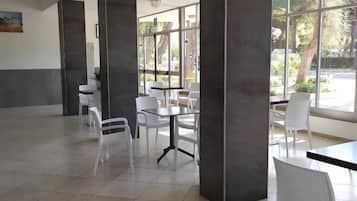 A spacious indoor area with large windows, white chairs, and tables arranged for dining or meetings.
