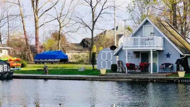 A house with a balcony, a small shed, and a dock extending into a body of water. - Adorable Gun Lake Cottage (Shelbyville)