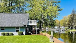 A house with a dock extending into a calm lake, surrounded by trees and other houses. - Adorable Gun Lake Cottage (Shelbyville)