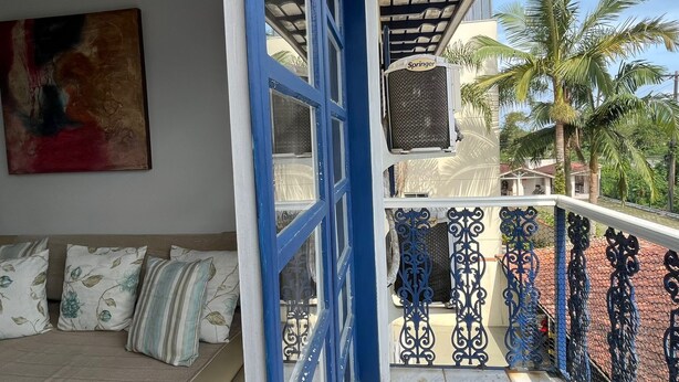 A balcony with a blue railing, a sofa with cushions, and a painting on the wall.