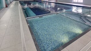 Une piscine dont le plafond est décoré d’une fresque représentant une forêt, avec un sol carrelé et une eau cristalline.