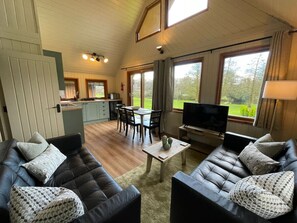 A cozy living room with a sofa set, a coffee table, and a TV. There is a dining area with a table and chairs. - RoseTree Lodge 3 bed Sleeps 6 (Hengar Manor Holiday Park)