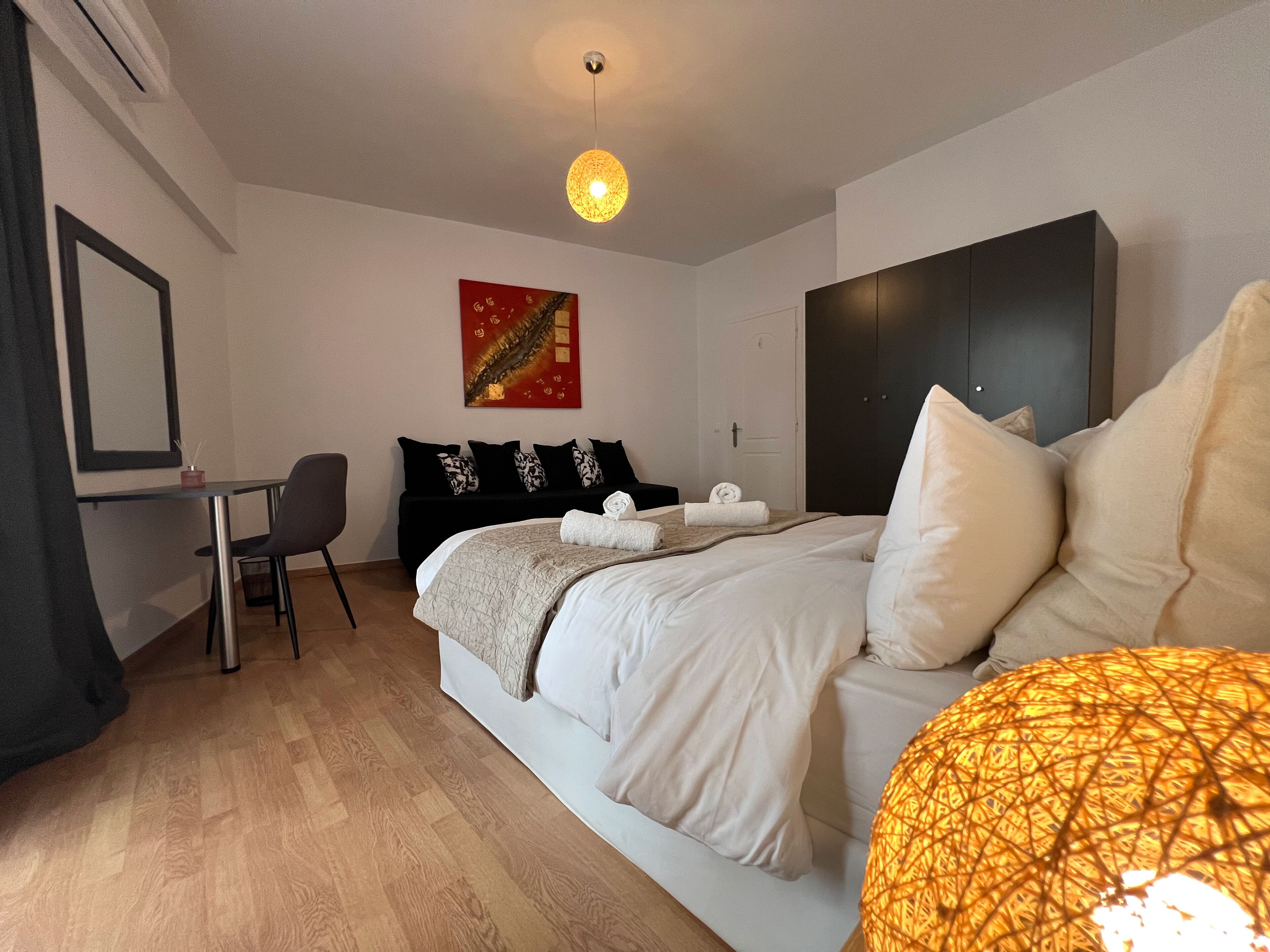 Quarto de hotel com cama, mesa de cabeceira, cadeira, escrivaninha e um quadro na parede.