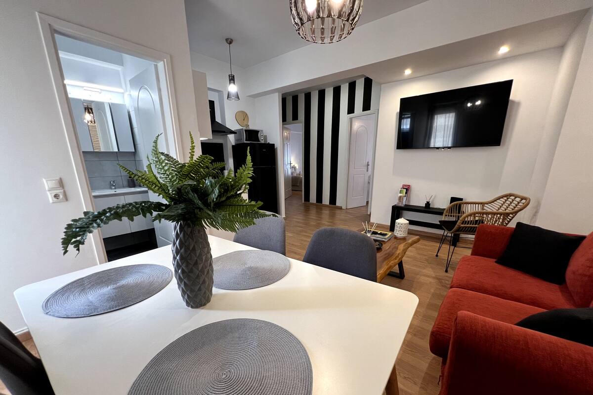 A modern living room with a white dining table, red sofa, and a TV mounted on the wall.