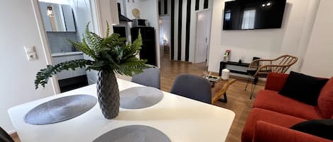 Un moderno salón con una mesa de comedor blanca, un sofá rojo y un televisor montado en la pared.