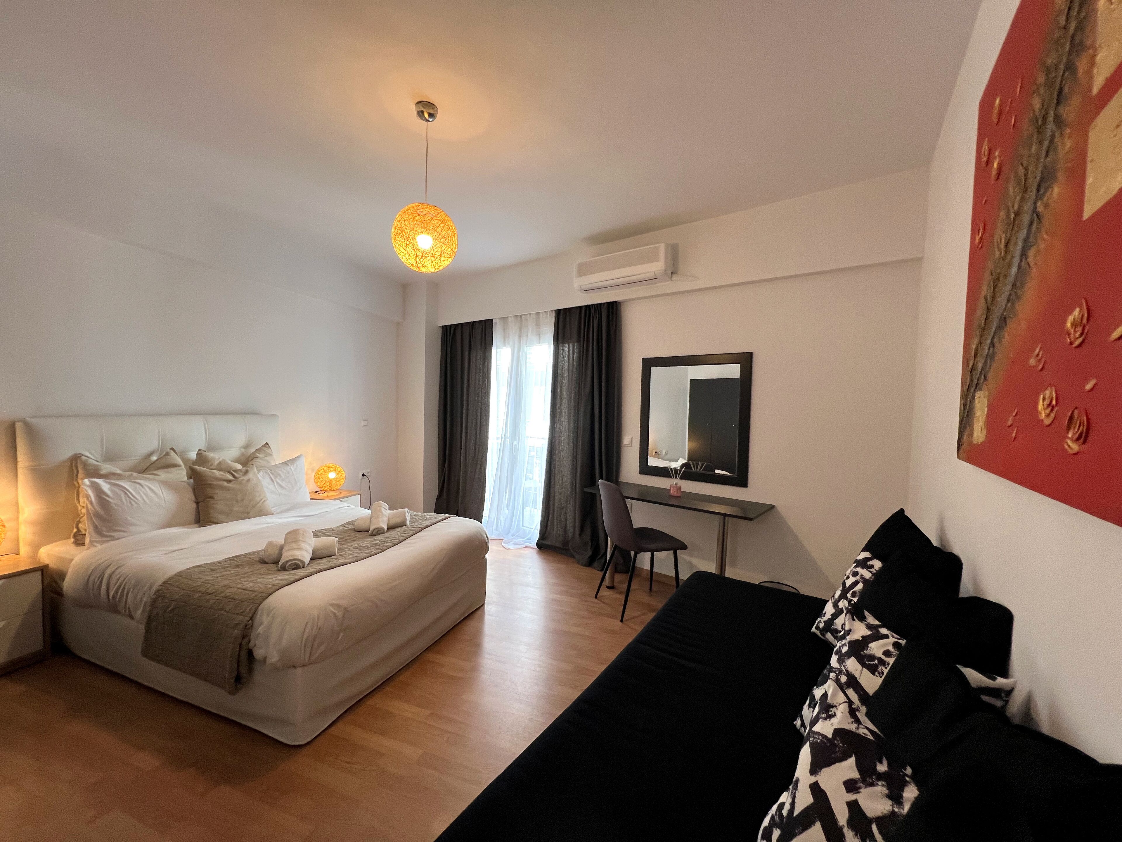 Et hotelværelse med seng, skrivebord, stol, sort sofa og et maleri på væggen.