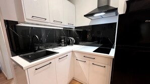 A modern kitchen with white cabinets, a black refrigerator, and a black stove. - Allure Athens Urban Suites (Athens)
