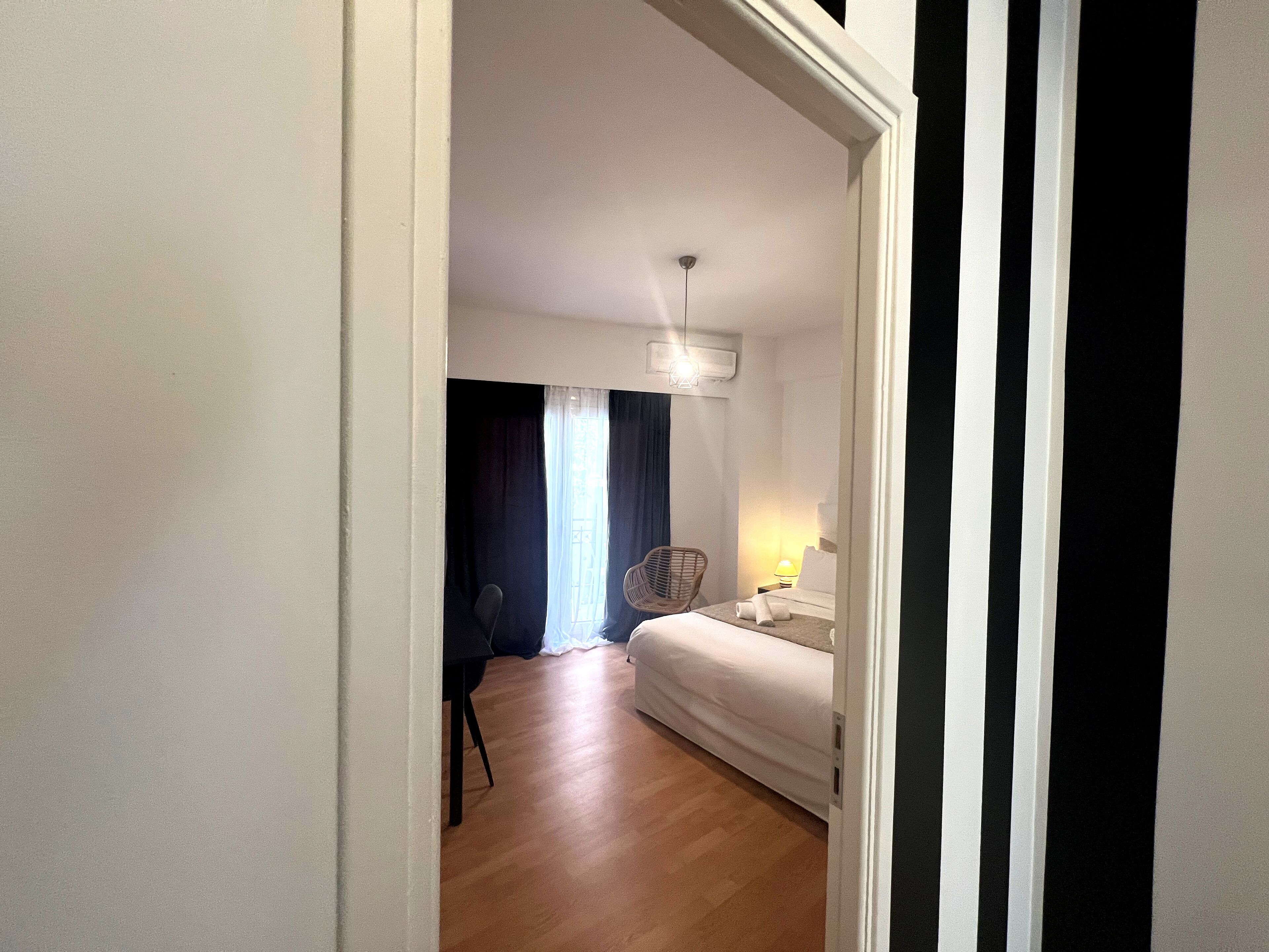 A hotel room with a bed, a chair, a desk, a lamp, and a window with curtains.
