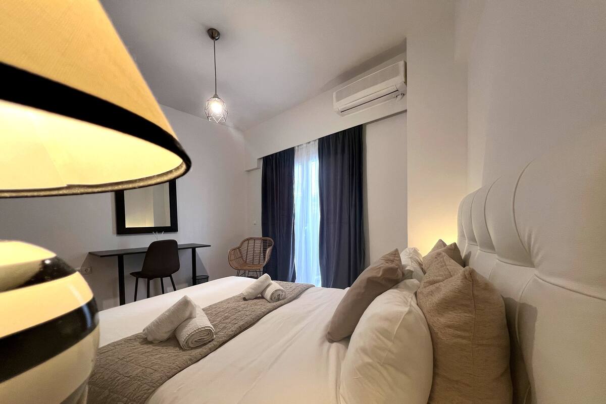 A hotel room with a bed, a desk, a chair, and an air conditioning unit.