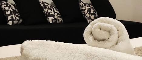 A neatly made bed with a rolled white towel, a patterned blanket, and a red abstract painting on the wall.