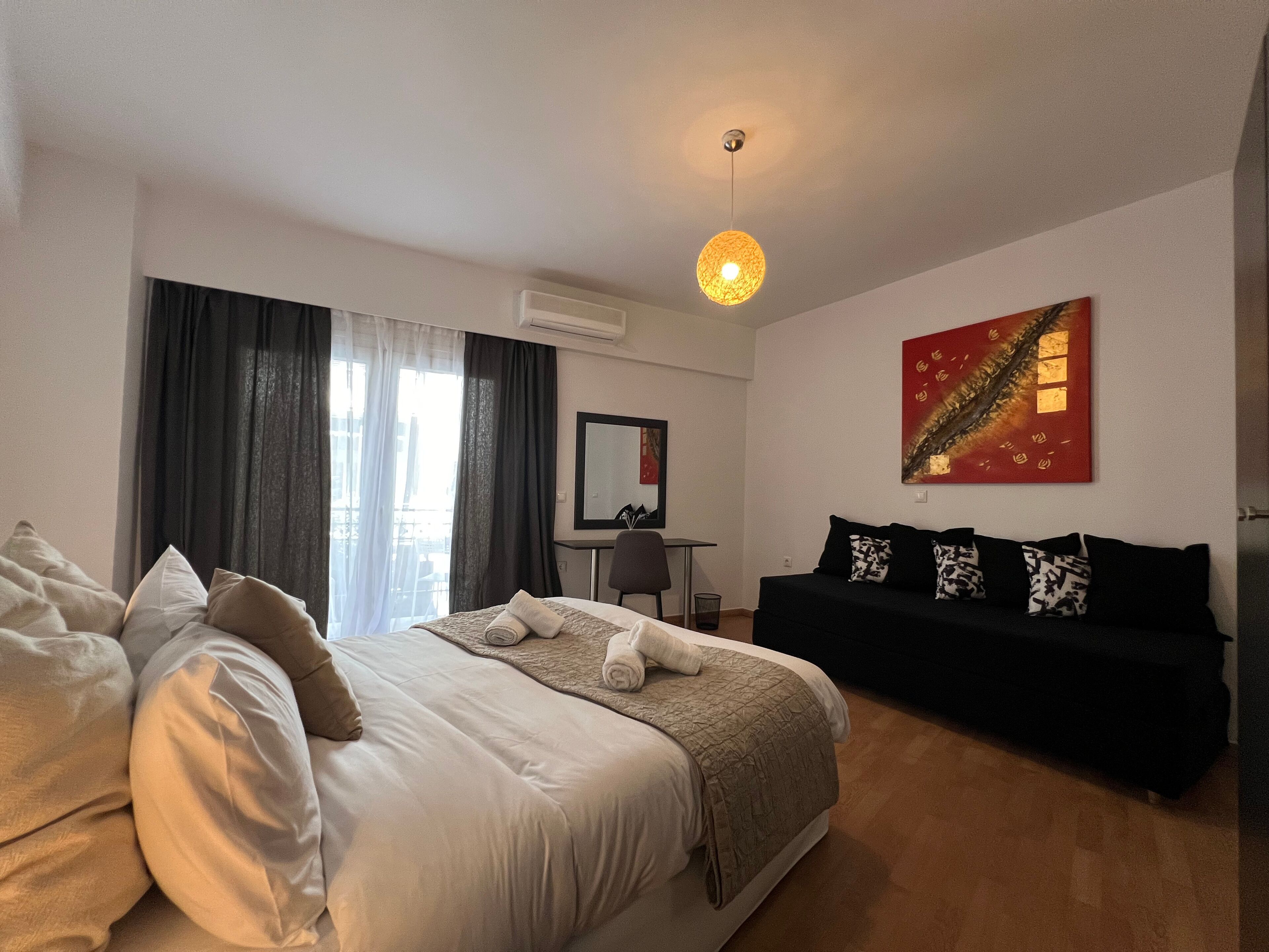 Une chambre d’hôtel avec un lit, un canapé noir, un bureau et une grande fenêtre avec des rideaux.