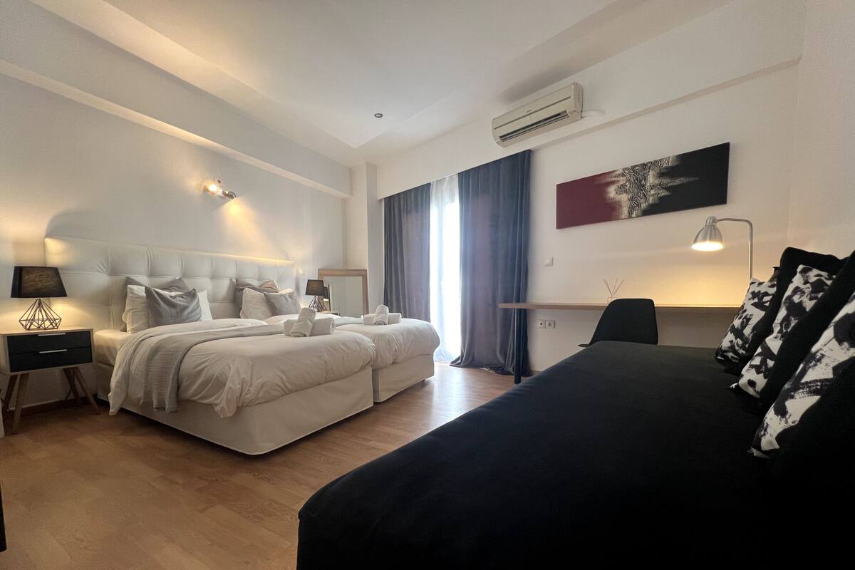 A modern hotel room with a large bed, a smaller bed, a desk, and a chair.