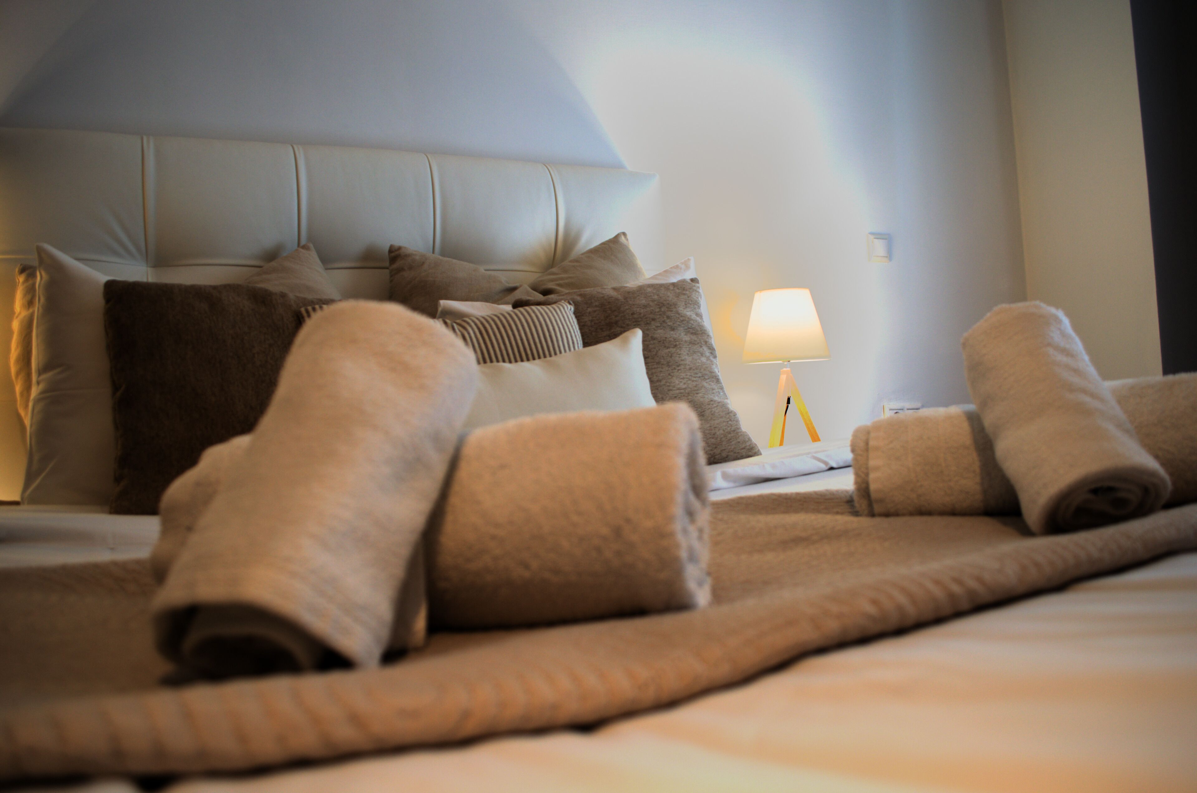 A neatly made bed with rolled towels, a headboard, and a bedside lamp.