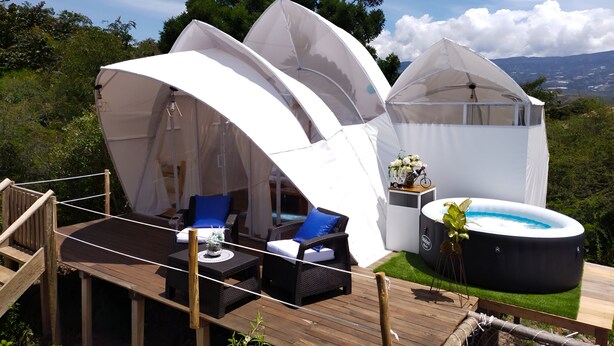 Un entorno exterior lujoso con terraza de madera, carpas blancas y un jacuzzi.