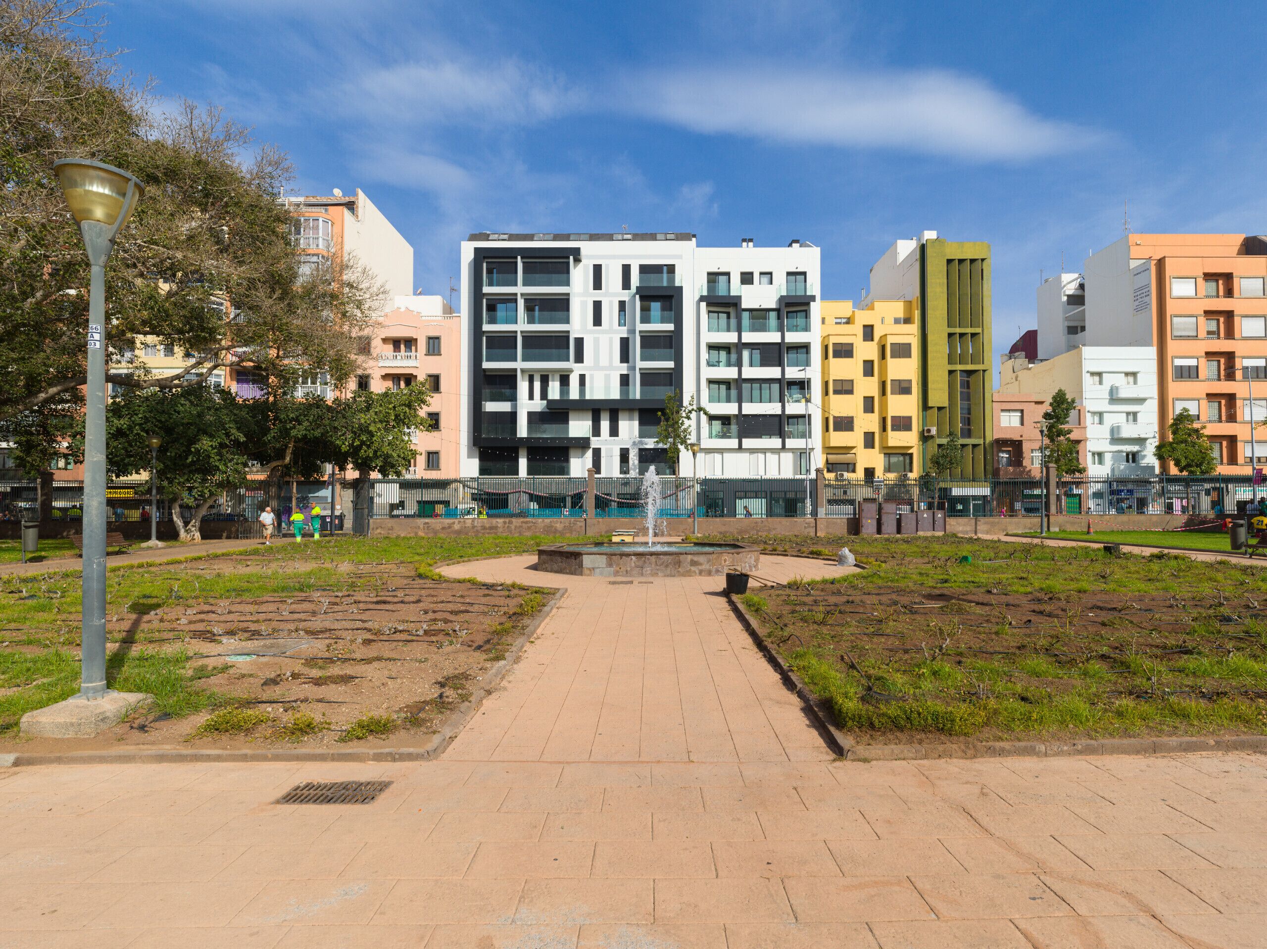A paved walkway leading to a modern building complex with multiple floors and balconies.