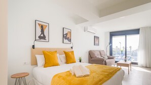 A modern hotel room with a large bed, a sofa, a small table, and a view of the city.