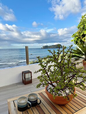 A wooden table with two mugs and a potted plant on a balcony overlooking the sea. - Cosy house with a magnificent ocean view and the most famous landmark in Azores (Vila Franca Do Campo)