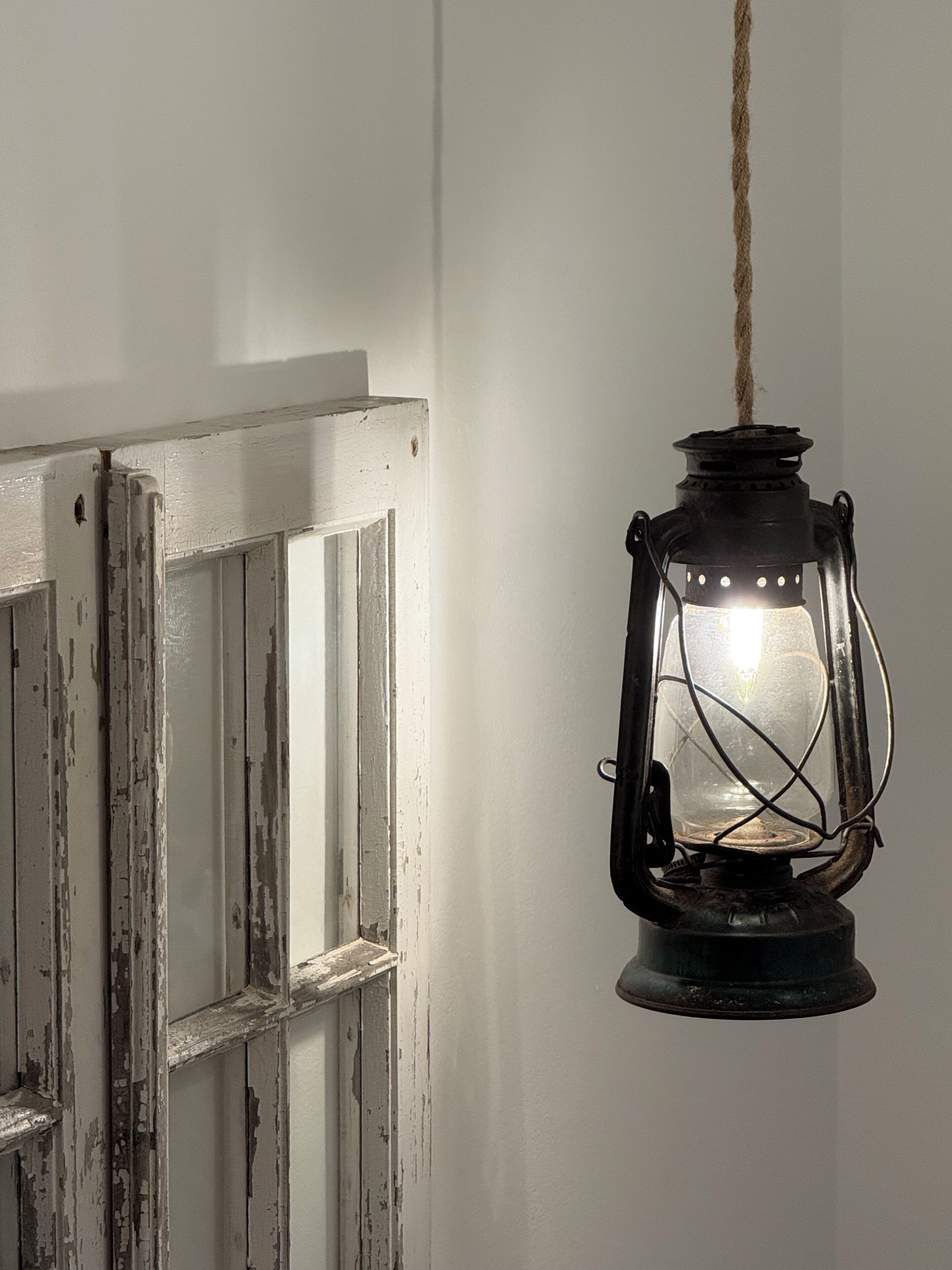 A rustic lantern hanging from a rope against a white door with peeling paint.