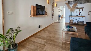 Un salon spacieux doté d’un parquet, d’un téléviseur à écran plat fixé au mur et d’un canapé de couleur sombre.