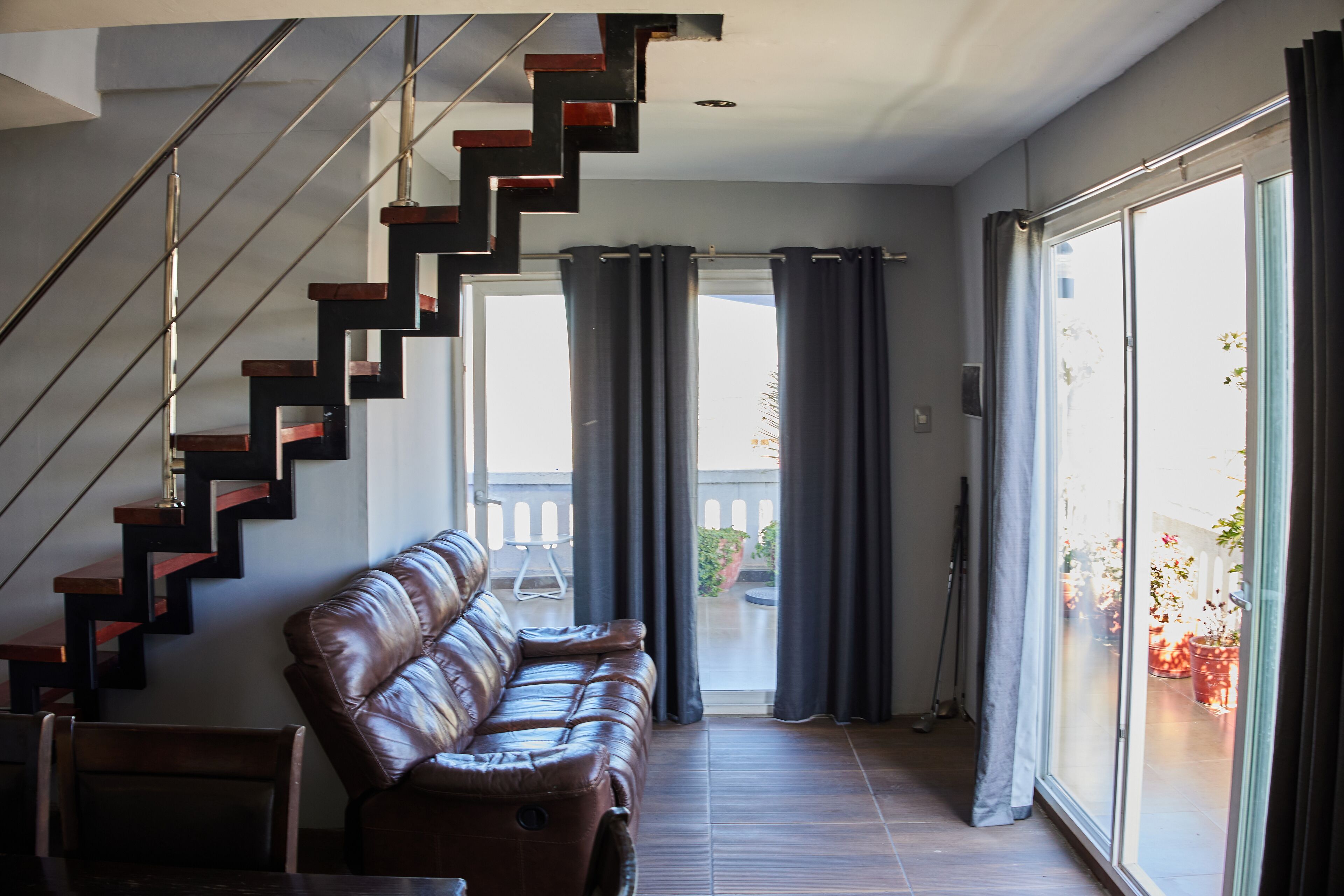 Un interior moderno con un sofá de cuero, una escalera y vistas a un espacio exterior con plantas en macetas.