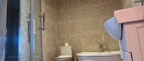 A modern bathroom with a glass-enclosed shower, a white toilet, a white bathtub, and a pink vanity.