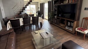 Una sala de estar moderna con un sofá, una mesa de centro, otomanas, un televisor y una escalera que lleva a un balcón.