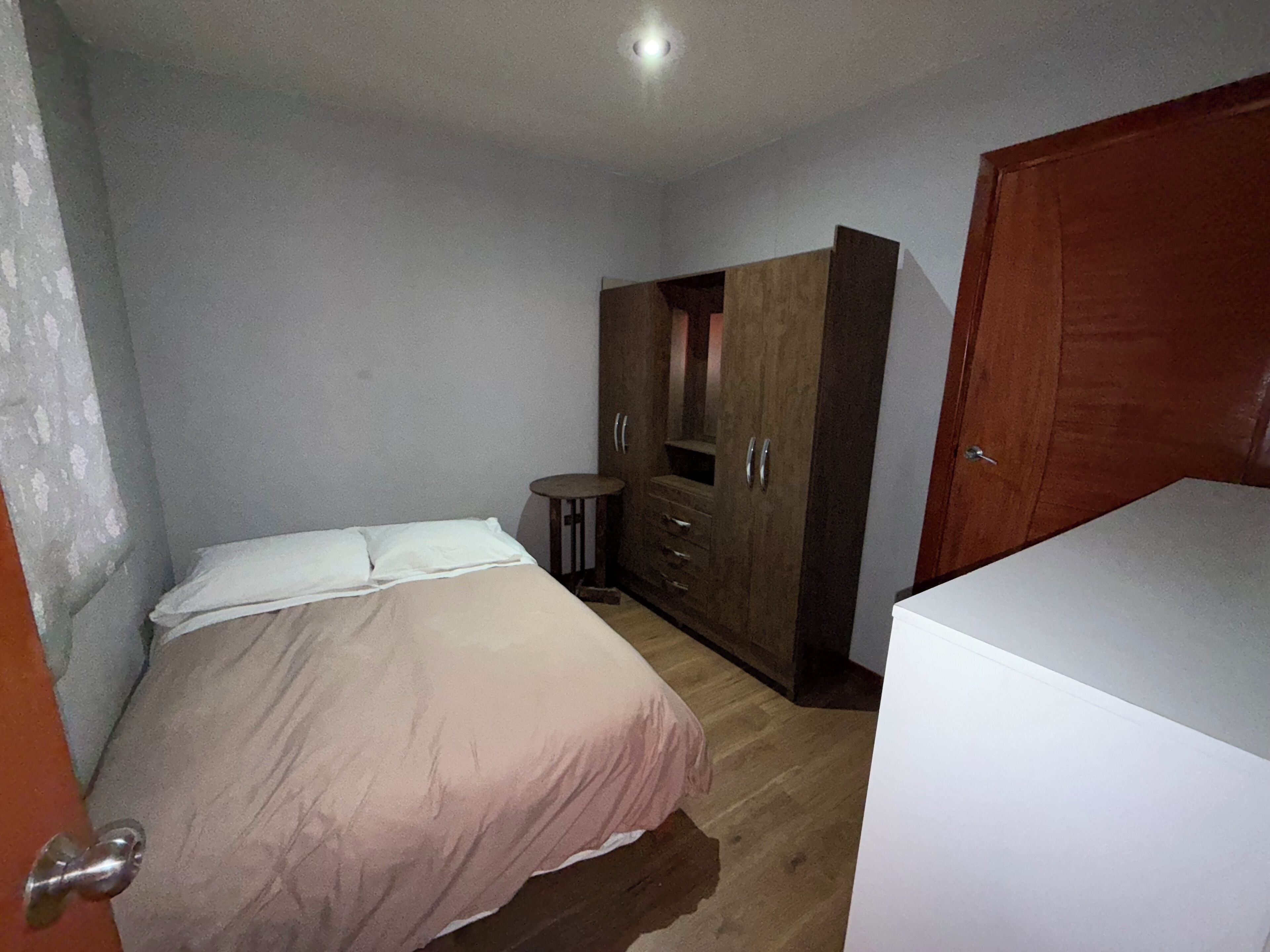 A bedroom with a bed, a wardrobe, and a small table.
