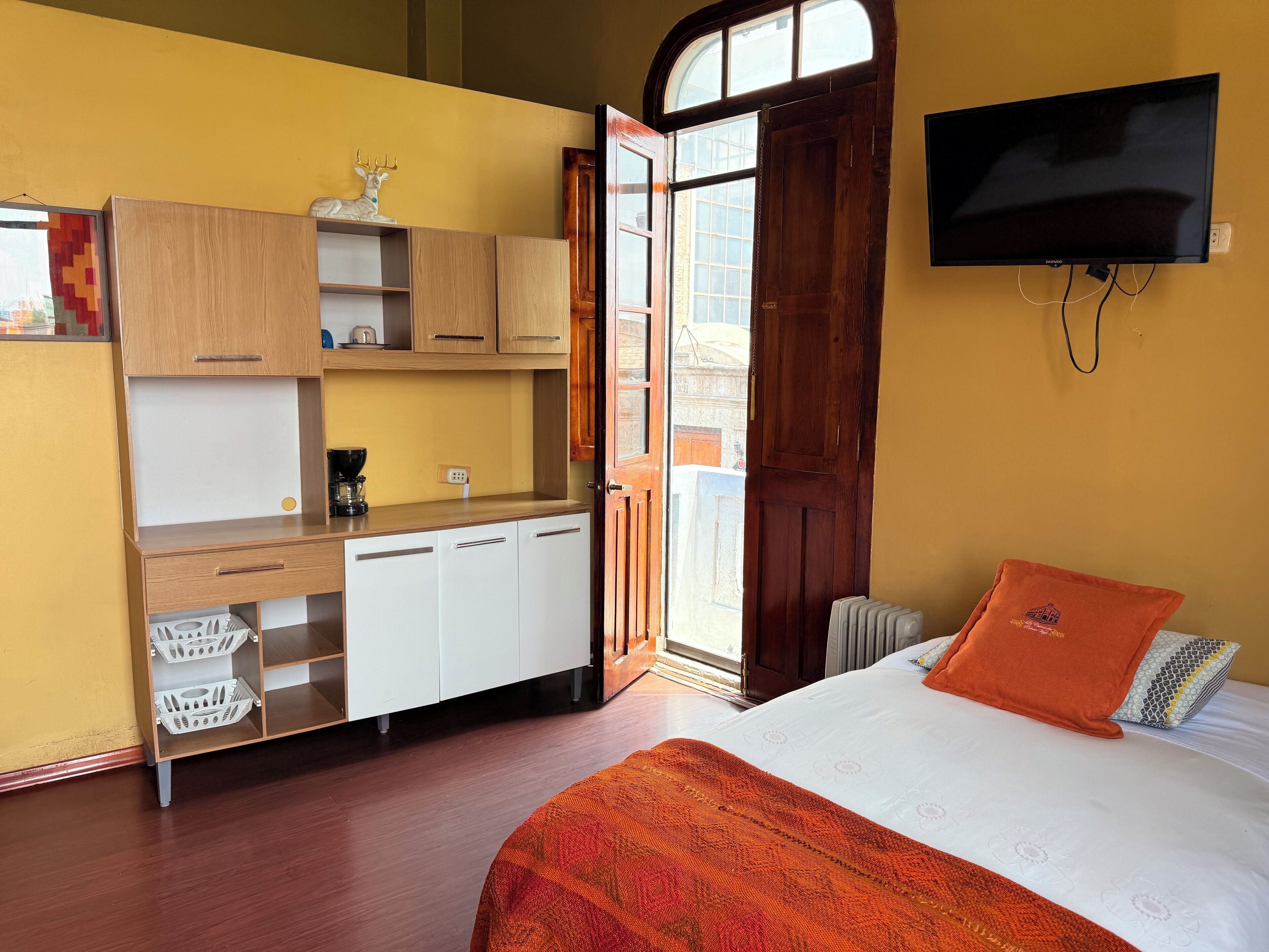 Una habitación pequeña con cama, televisión, escritorio de madera con estante y ventana.