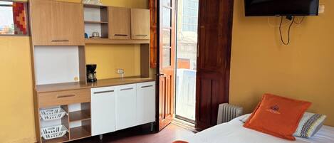 Una habitación pequeña con cama, televisión, escritorio de madera con estante y ventana.