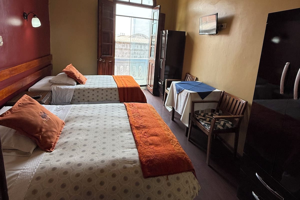 Une chambre d’hôtel avec deux lits, un bureau, une chaise, une télévision et une fenêtre donnant sur des immeubles.