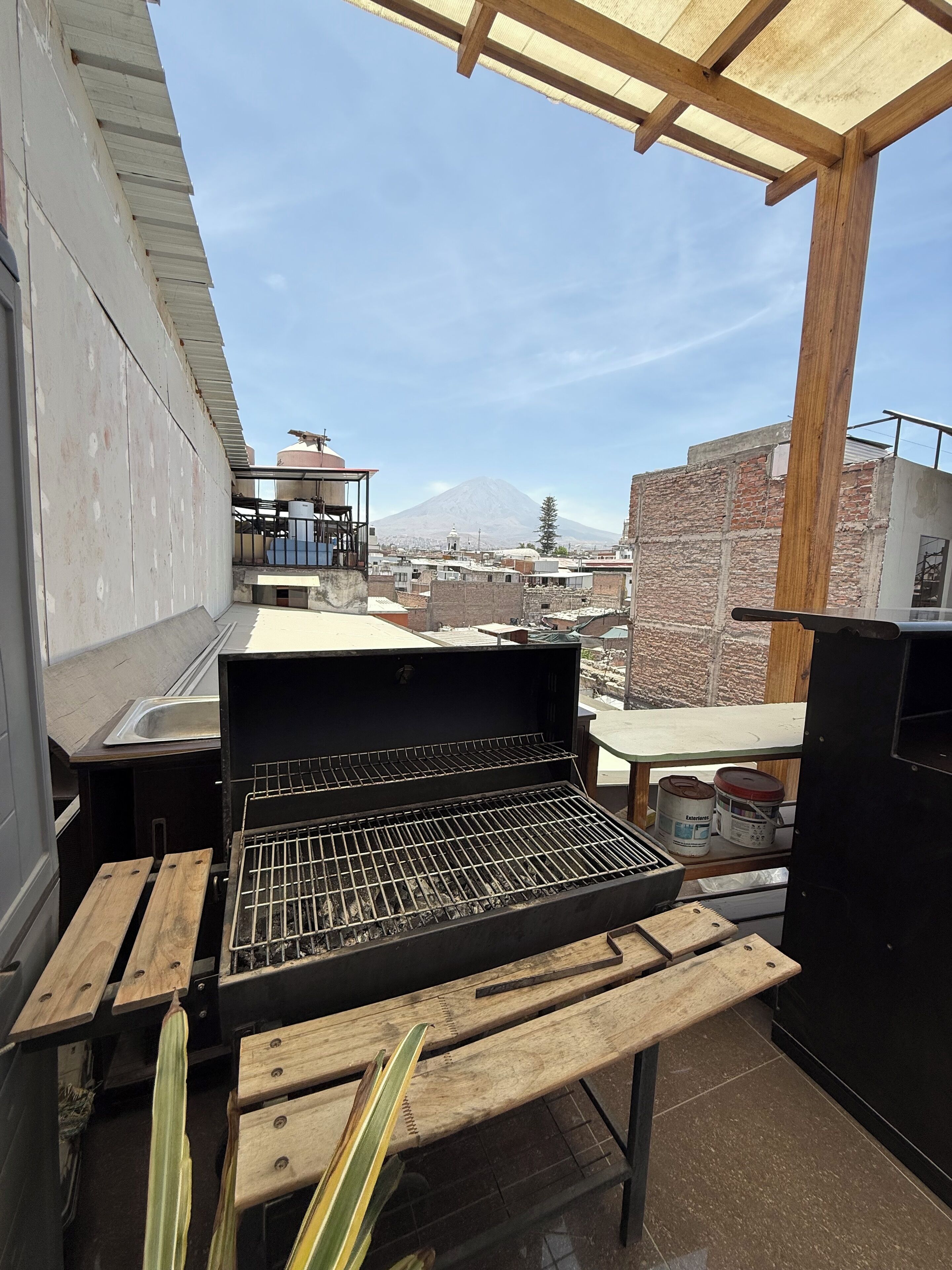 A rooftop with a grill, wooden benches, and a view of a mountain.